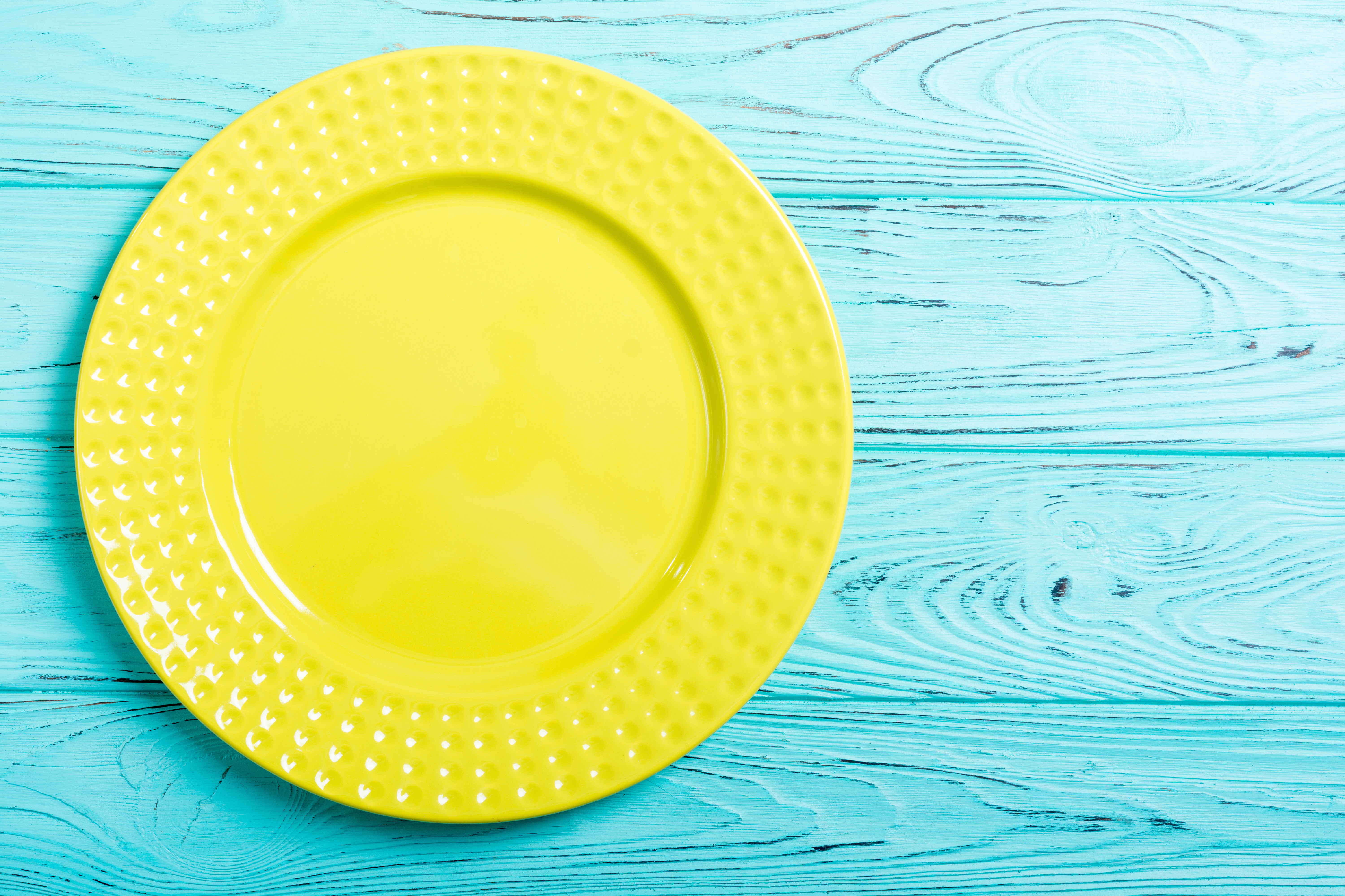 俯瞰の視点で、水色の木製テーブルの上に黄色の平皿が一枚